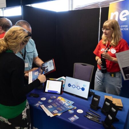 Attendee receiving information from exhibitor at a booth with blue display.