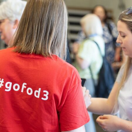 Back view of attendee wearing a red event shirt with printed hashtag 
