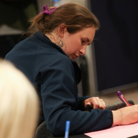 Person writing notes attentively during a session, leaning over a table.