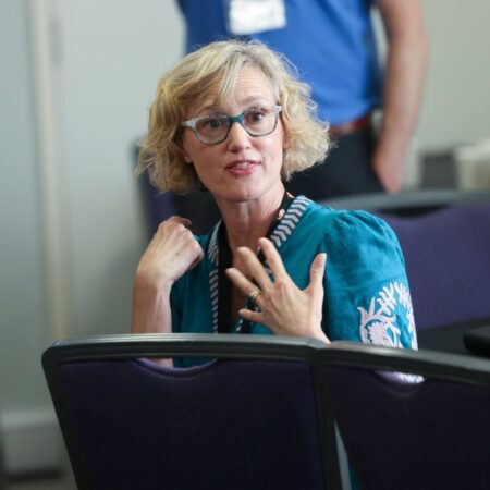 Attendee speaking thoughtfully in a seated discussion, hand on chest.