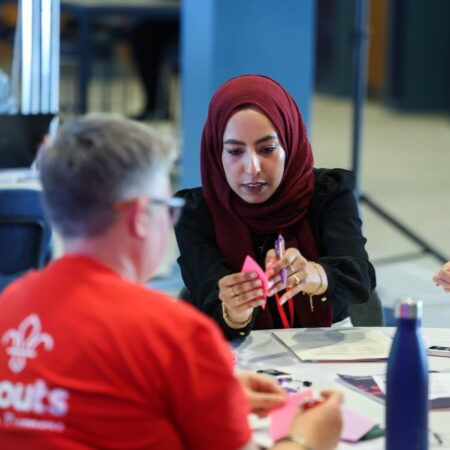 Person wearing a red hijab concentrating while writing or assembling something at a table with others.