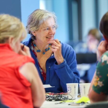 Person smiling and engaged in conversation at a table with another person partially visible.