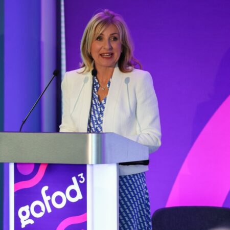 Person speaking at a podium with a purple “gofod3” banner behind.