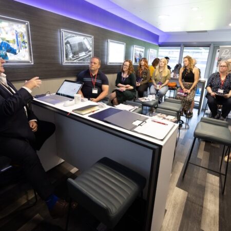 Presenter speaking at podium with event branding in background.