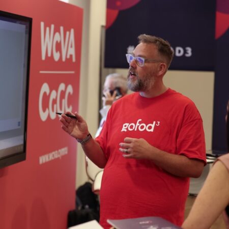 Exhibitor standing near booth with red banner and promotional items.